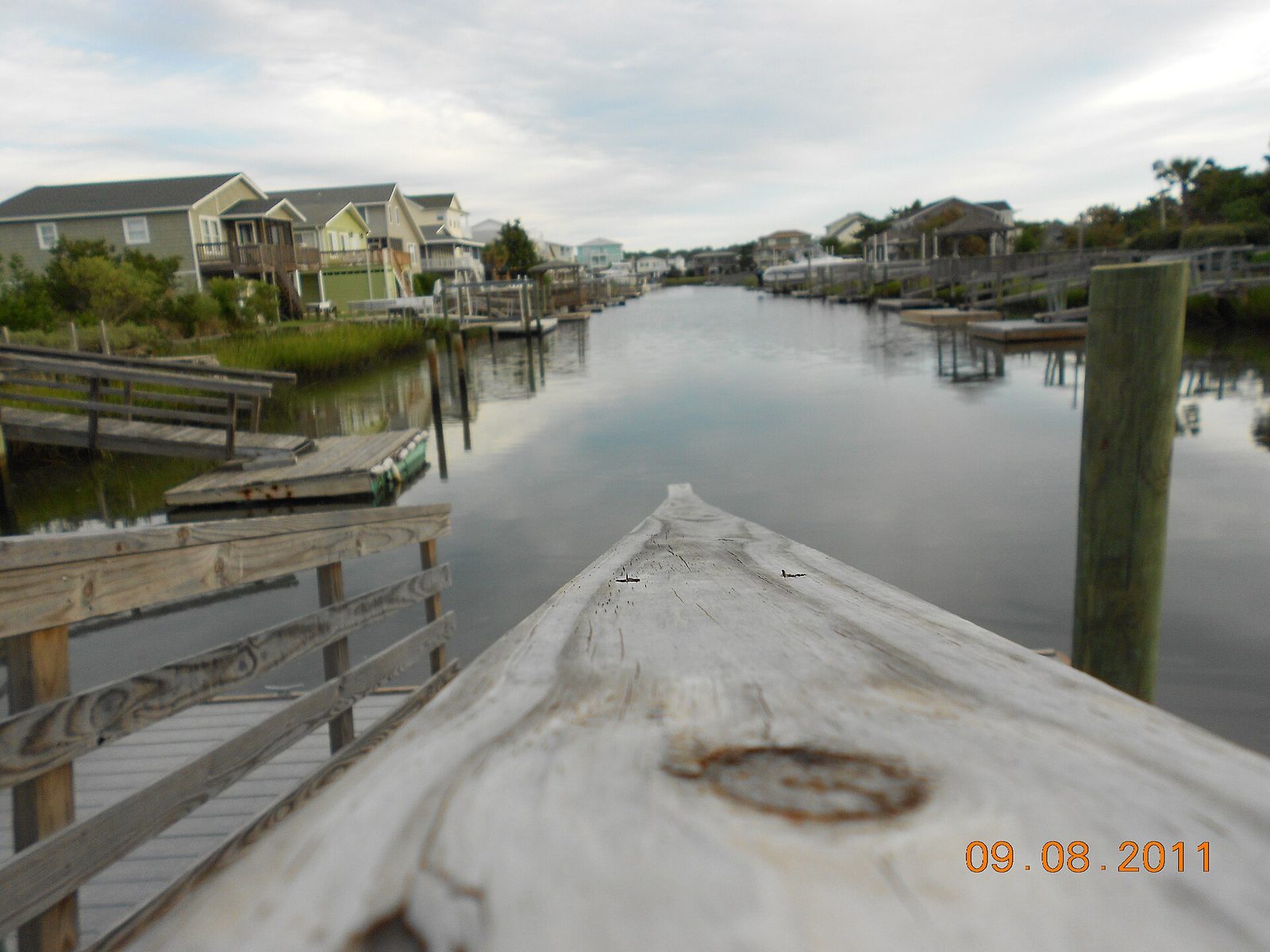 A still canal behind Holden Beach homes, seen from the end of a wooden dock